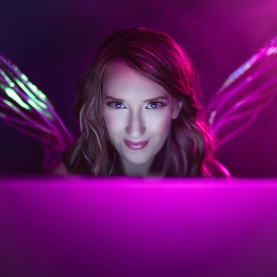 Jennifer in front of a laptop computer looking straight ahead. Her face lit by the screen. She has fairy wings on her back.