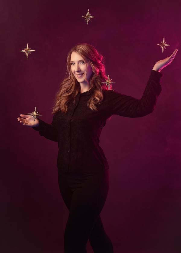 Jen standing in front of a dark purple background with arms out to the side and raised. Surrounded by several stars that she seems to be controlling with magic.